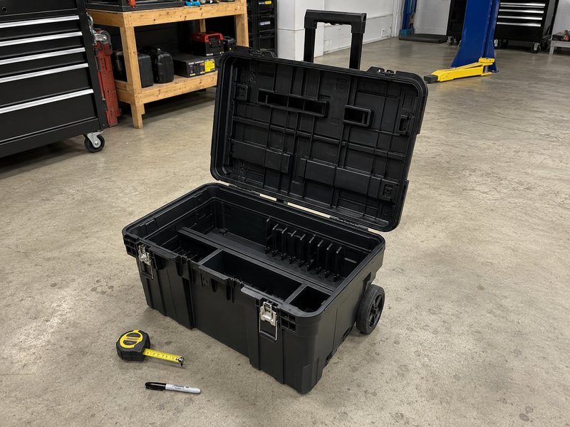 Empty black rolling toolbox with lid open on garage floor showing compartments and wheels